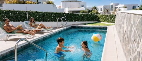 Una piscina con sillas de descanso, un muro de piedra y un cielo despejado.