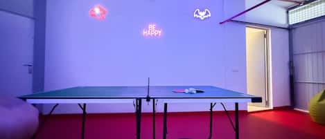 A ping pong table with neon signs in a room with red flooring.