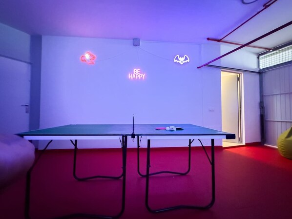 A ping pong table with neon signs in a room with red flooring.