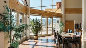 Un espace intérieur spacieux, doté de grandes fenêtres, d’un plafond en bois et d’une table à manger avec des chaises.