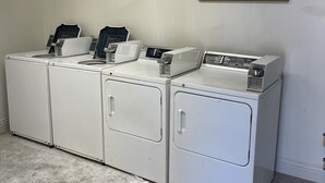 A laundry room with four white front-loading washing machines and a sign that reads "LAUNDRY ROOM self service." - Cozy Grain Bin Room Retreat on a Working Mini Farm (Augusta)