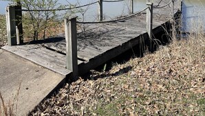 A wooden pier with a gazebo at the end, surrounded by a chain-link fence, leading to a calm lake with a forest in the background. - Cozy Grain Bin Room Retreat on a Working Mini Farm (Augusta)