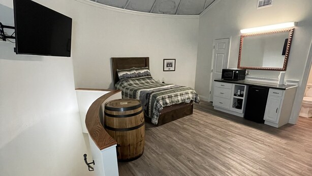 A bedroom with a bed, a wooden barrel, a desk with a mirror, and a staircase. - Cozy Grain Bin Room Retreat on a Working Mini Farm (Augusta)