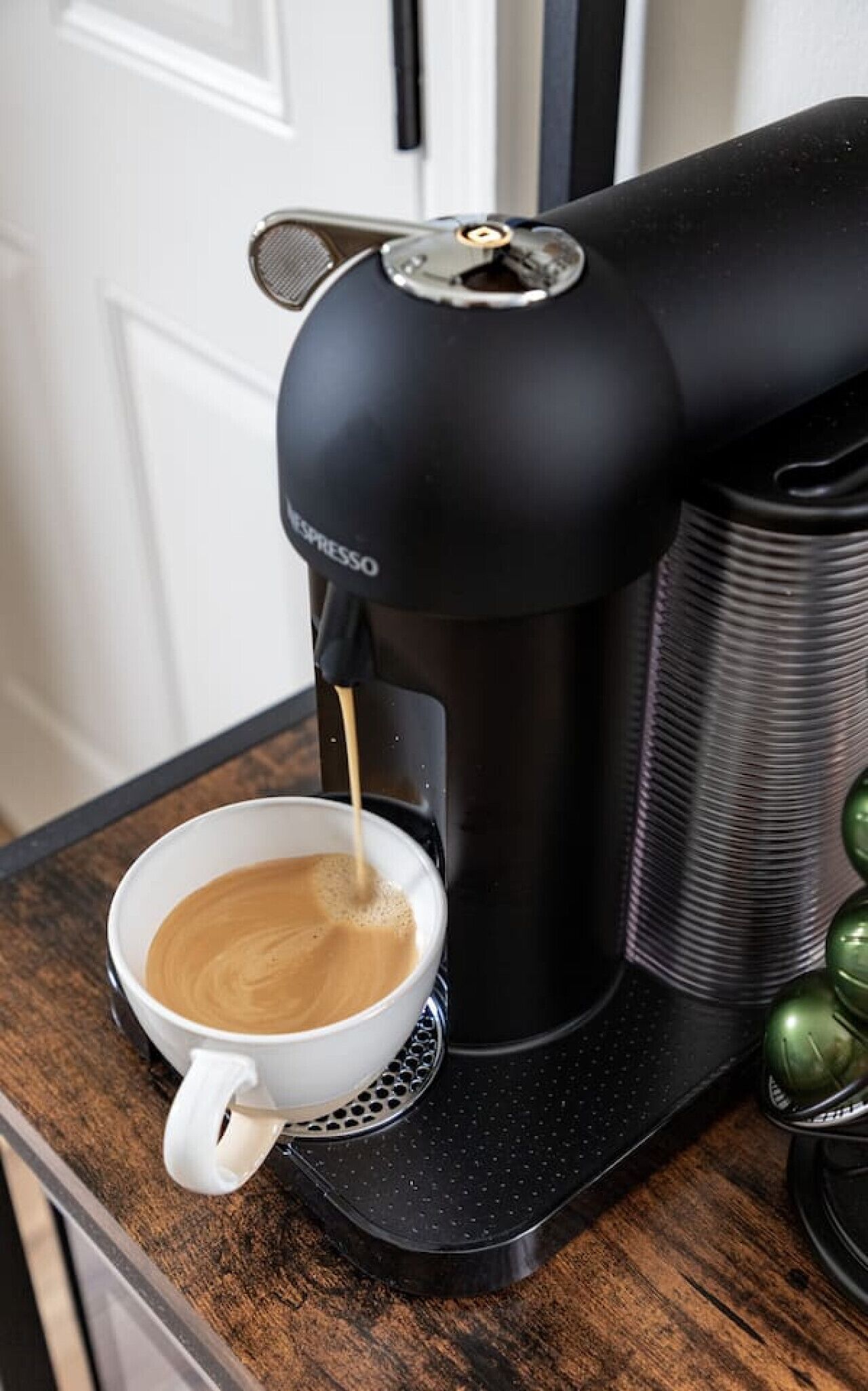 A black espresso machine dispensing coffee into a white cup on a wooden countertop.