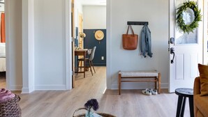 Un salon avec un banc, une table basse, une porte décorée d’une guirlande et un couloir menant à une salle à manger.