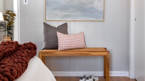 Een slaapkamer met een bed, een bankje, een vloerkleed en een aan de muur hangend schilderij.