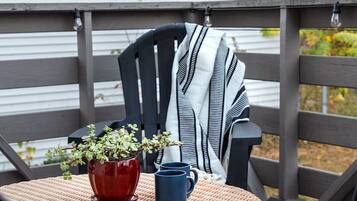 A wicker table with a potted plant and two mugs on a deck with a chair.