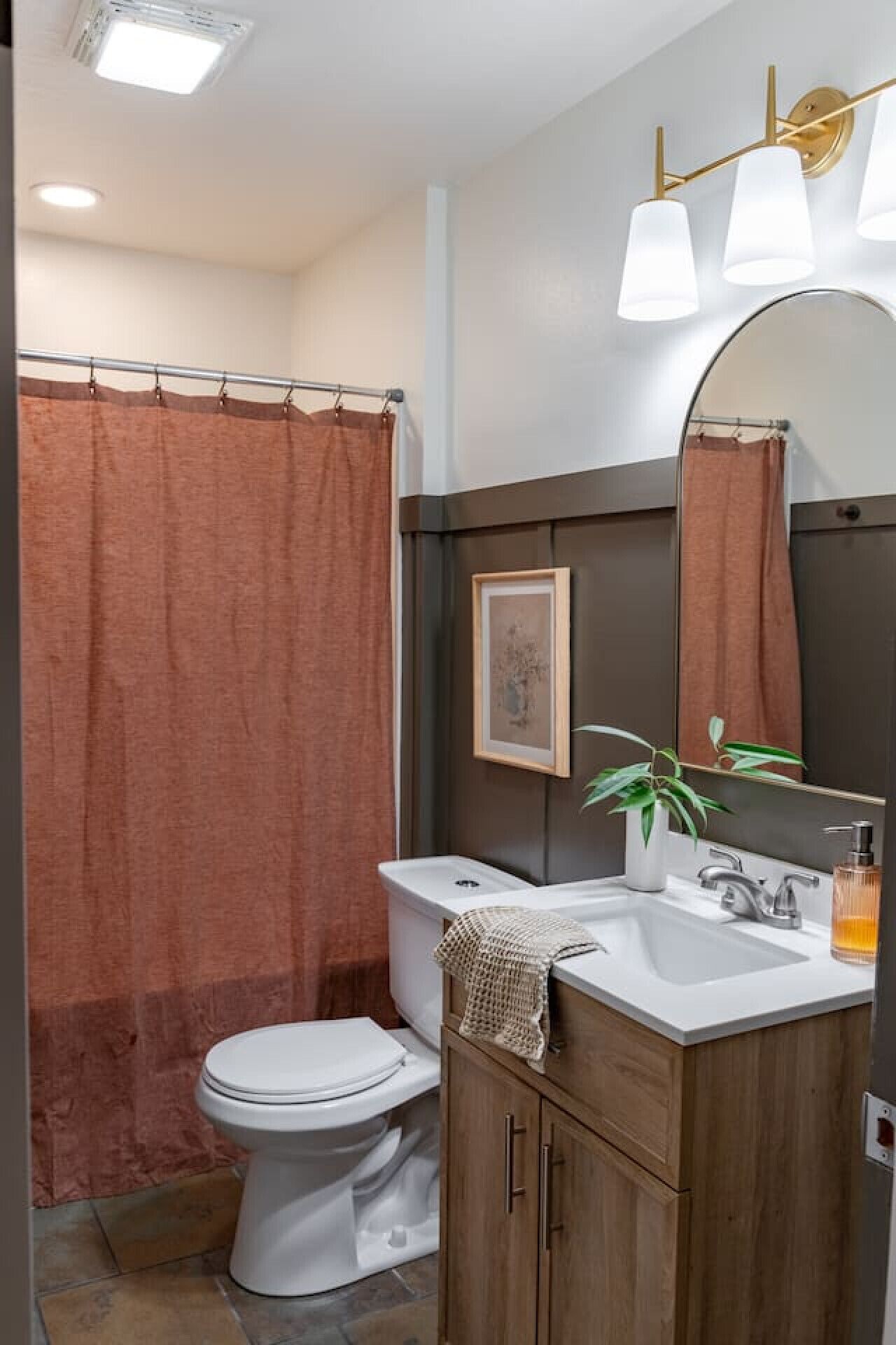 A bathroom with a shower curtain, toilet, sink, mirror, and a plant.