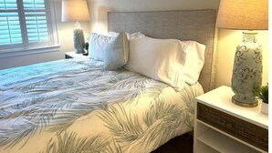 Un lit bien fait, recouvert d’une couvre-lit à motifs de feuilles, avec deux lampes de chevet et un vase décoratif posé sur une table de chevet.