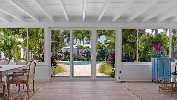 A spacious room with a large sliding glass door leading to a pool area, a dining table with chairs, and a blue cabinet.