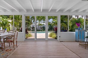 Amplia habitación con un gran ventanal corredero que da a una zona de piscina, una mesa de comedor con sillas y un armario azul.