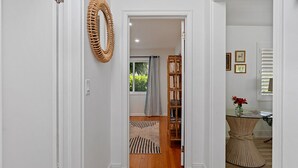 A hallway with a wooden floor, a woven rug, a wicker mirror, and a wooden bookshelf.