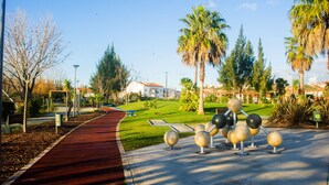 Un sendero en un parque con una pista de atletismo roja, palmeras y una escultura de esferas.