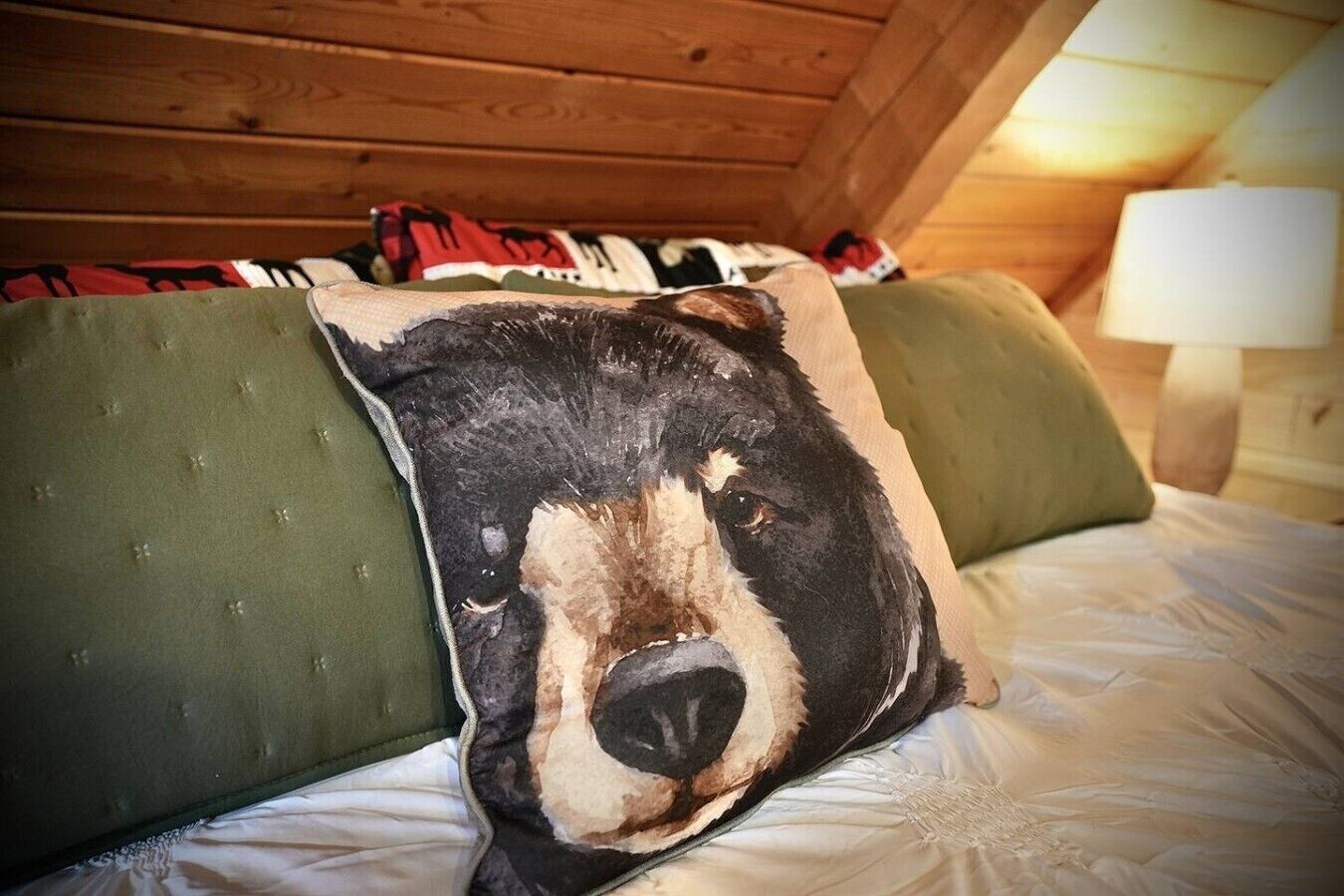 A bed with a pillow featuring a bear's face, green pillows, and a wooden ceiling.
