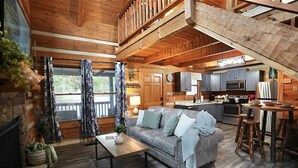 A rustic cabin interior with a loft bedroom, a kitchen, and a living area.