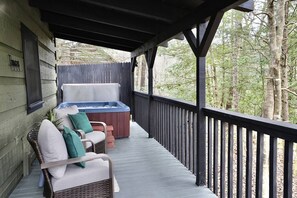 Une véranda abritée avec un jacuzzi, des fauteuils en osier et une vue sur les arbres.