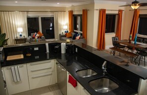 A modern kitchen with black countertops, stainless steel sinks, and a dining area with a wooden table and chairs.