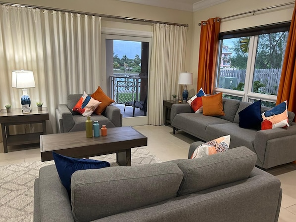 A modern living room with grey sofas, a coffee table, and a balcony with curtains.
