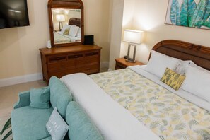 A hotel room with a bed, a dresser, a mirror, a TV, and a lamp.