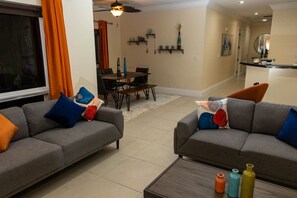 A living room with two grey sofas, a coffee table, and a dining area in the background.