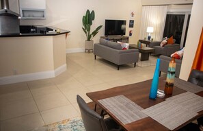A modern living room with a grey sofa, a TV, and a dining area with a wooden table and chairs.