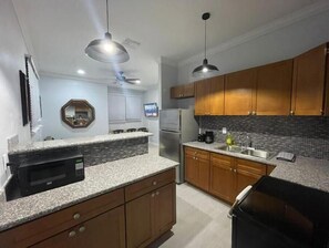 A modern kitchen with granite countertops, wooden cabinets, a built-in microwave, and a stainless steel refrigerator.