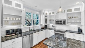 A modern kitchen with white cabinetry, a granite countertop, and a large window with a view of trees. - Luxury 4BR in Historic District, Walk to Downtown (Greenville)