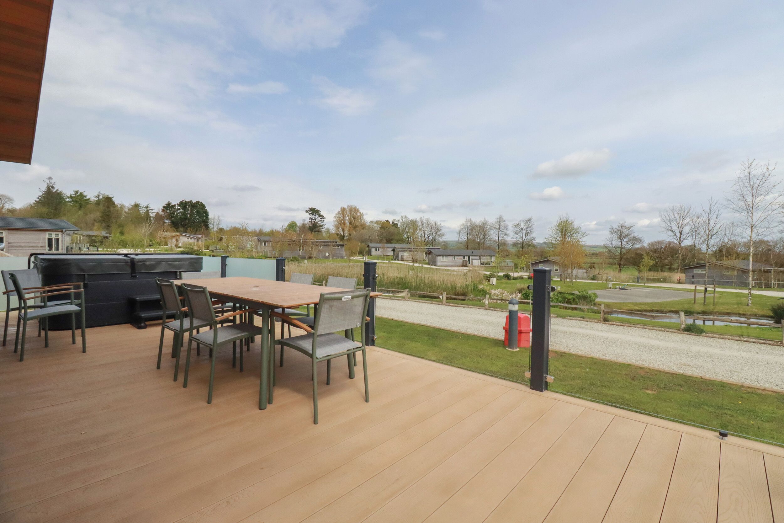 Eine Holzterrasse mit Tisch und Stühlen, mit Blick auf eine Rasenfläche, in deren Ferne eine Straße und Häuser zu sehen sind.