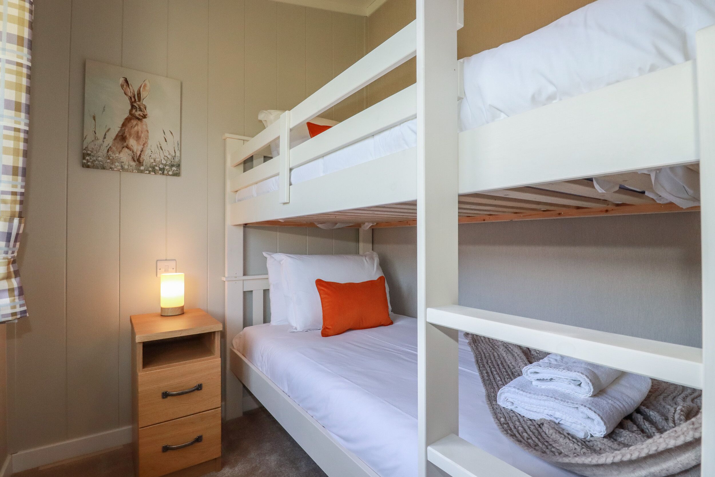 Une chambre avec un lit superposé, une table de chevet, une lampe et un tableau au mur.