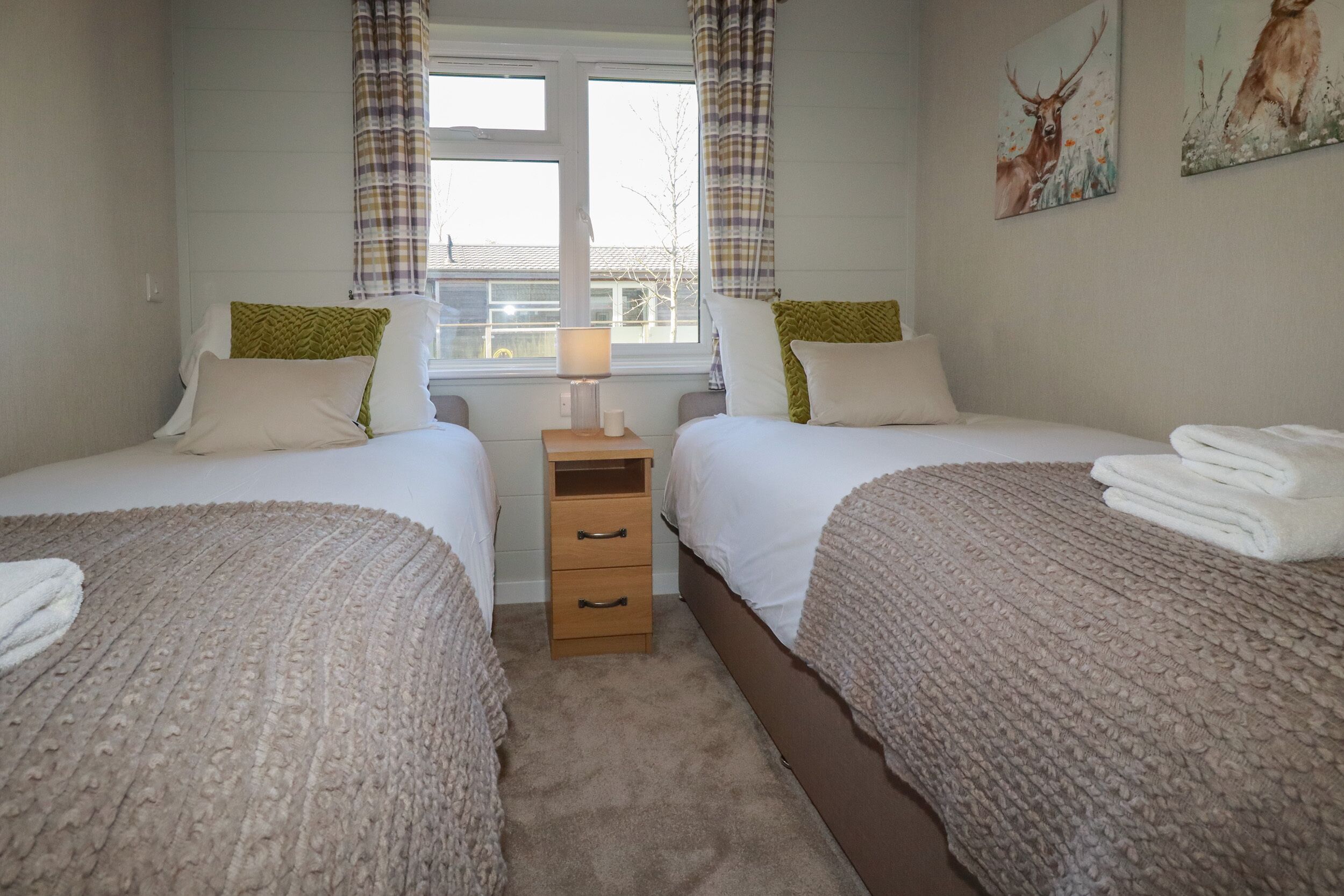 A bedroom with two beds, a nightstand, a lamp, and a window with curtains.