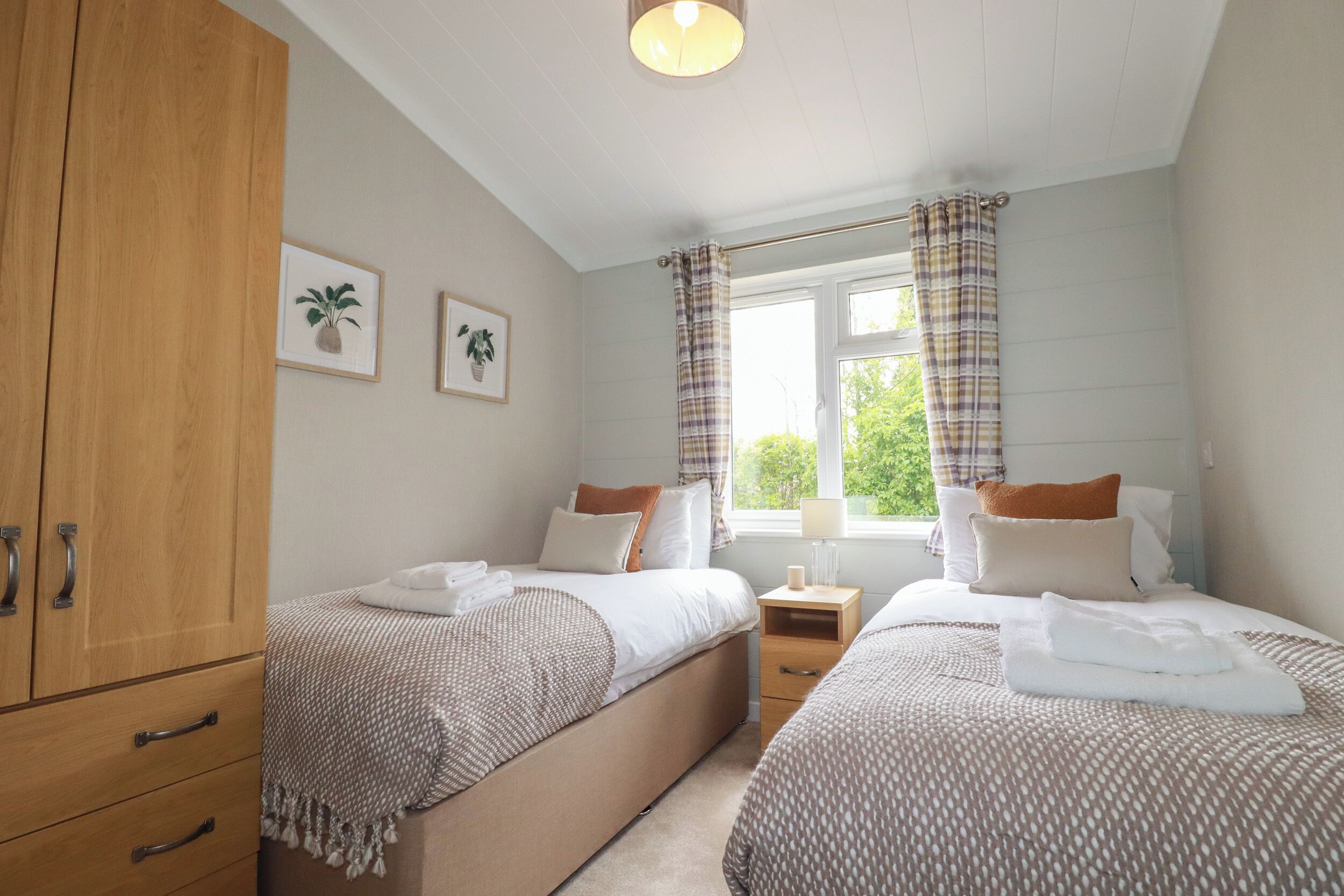 A bedroom with two beds, wooden wardrobe, and a window with curtains.