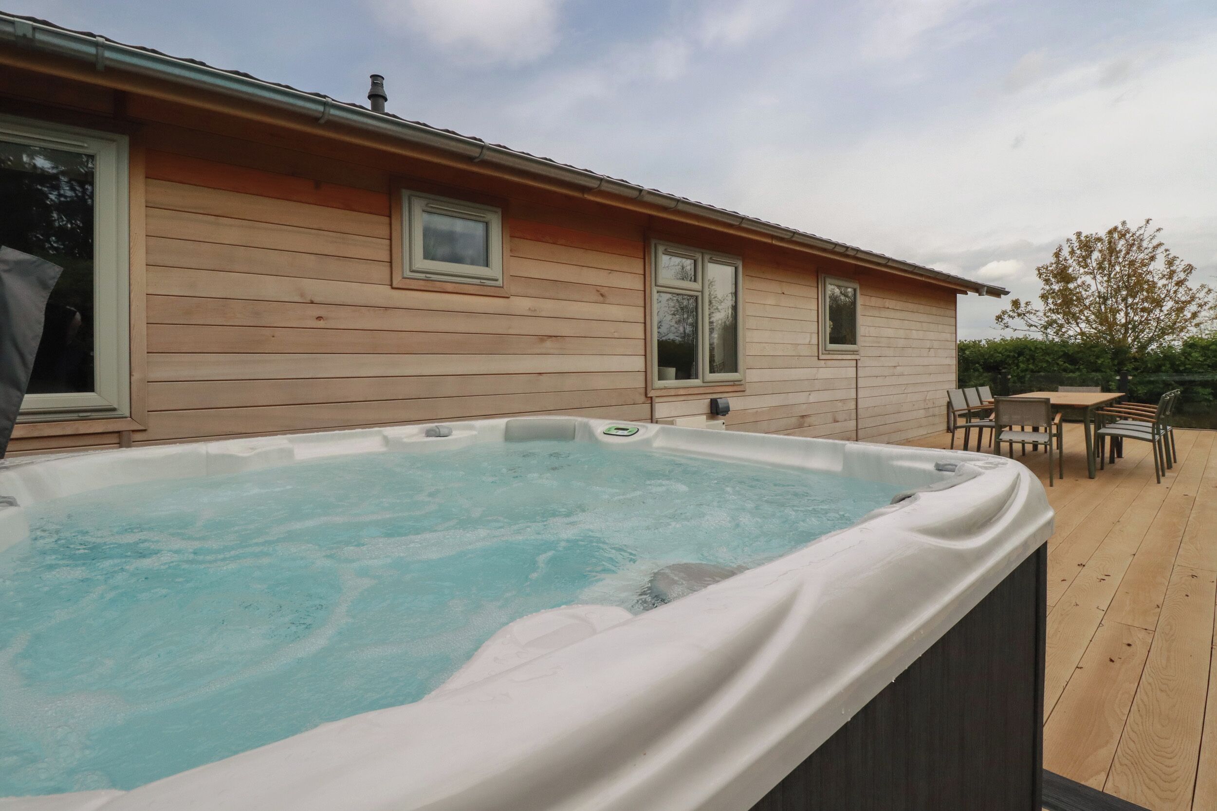 Un jacuzzi en una terraza de madera, con una casa al fondo.