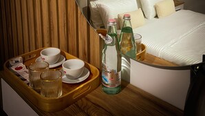 Une chambre d’hôtel moderne avec un grand lit, une tête de lit en bois et un plateau de petit-déjeuner comprenant des tasses, des bols et des bouteilles.