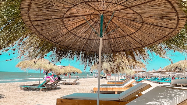 Une plage avec des chaises longues en bois et des parasols en chaume.