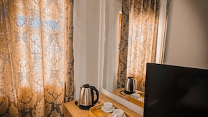 Une chambre d’hôtel compacte comprenant un bureau en bois, une bouilloire, un plateau avec des tasses et des verres, un petit réfrigérateur et un téléviseur.
