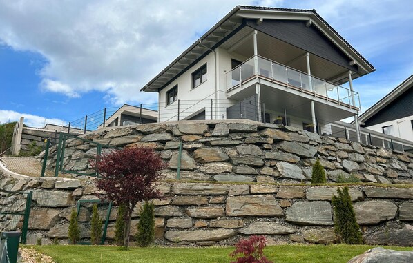 A modern two-story house with a stone retaining wall, a balcony, and a clear sky. - Chalet mit Karawankenblick (Köttmannsdorf)