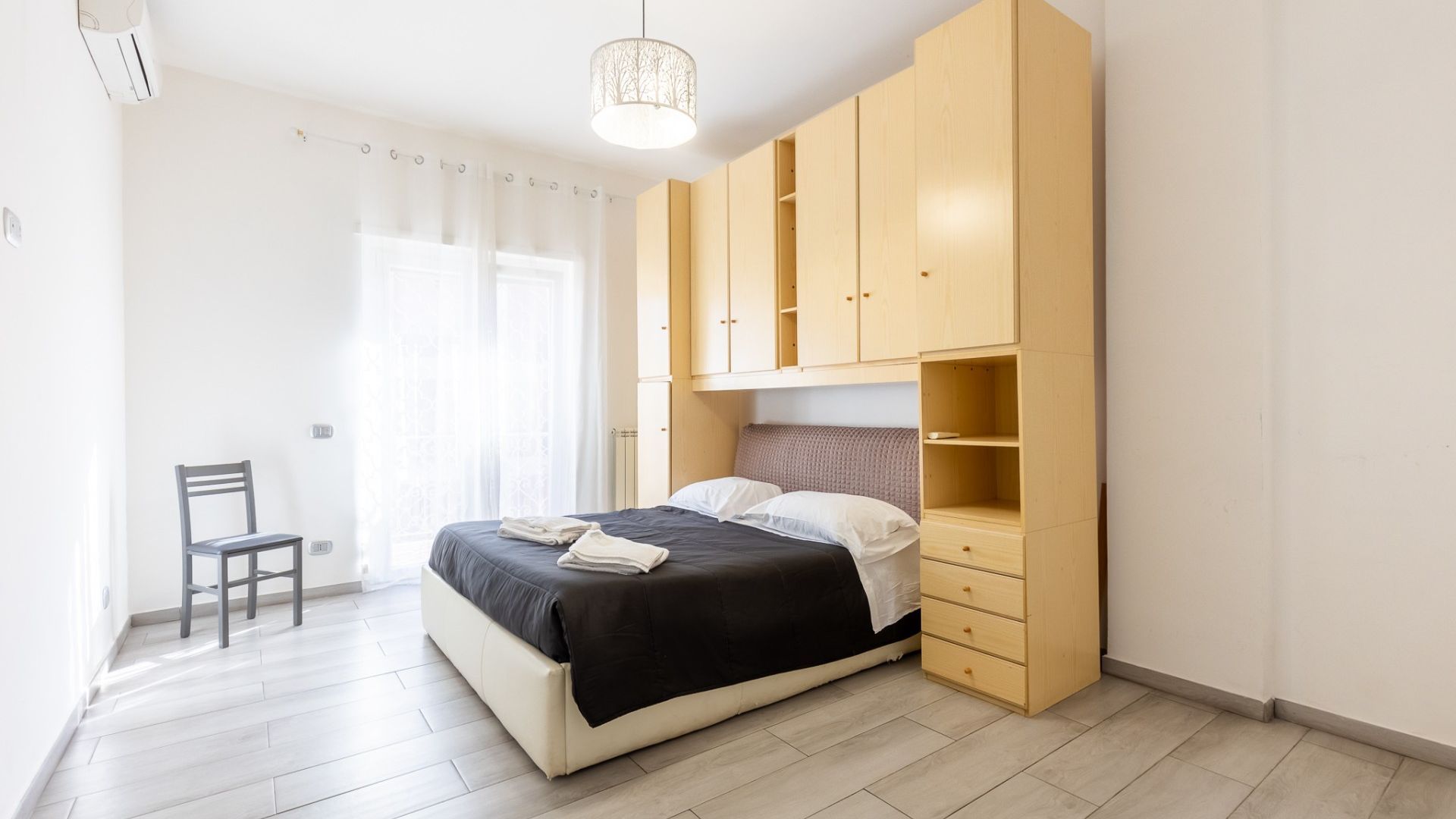 A bedroom with a bed, a chair, and built-in wooden storage cabinets.