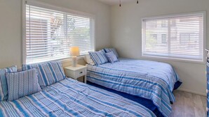 Une chambre avec deux lits, un ventilateur de plafond et de grandes fenêtres équipées de stores.