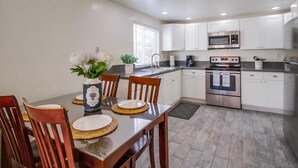 Une cuisine moderne avec des meubles blancs, des appareils en acier inoxydable et un coin repas agrémenté de chaises en bois et d’un vase de fleurs.