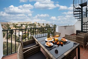 Enjoy a meal on the balcony with a view of the coastal town, featuring a table set with plates, glasses, and fresh fruit.