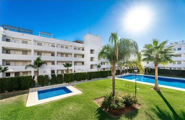 Un hotel de varios pisos con piscina, palmeras y césped bien cuidado.