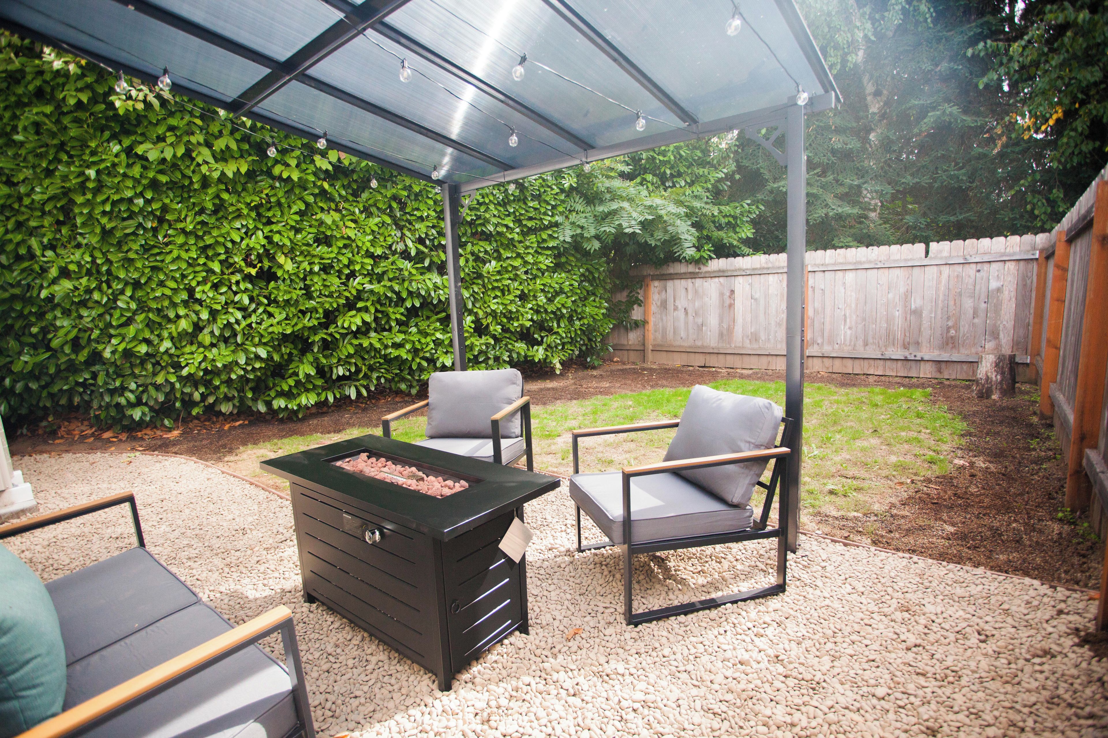 Een terras buiten met een barbecue, twee stoelen en een tafel.