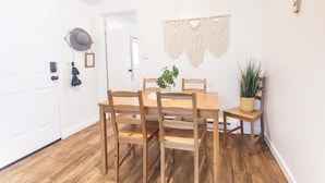 Un comedor con mesa y sillas de madera, un tapiz de macramé y una planta en maceta.