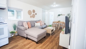 Una sala de estar moderna con sofá, reposapiés y mesa de centro, un comedor con mesa y sillas, y una cocina con estufa y armarios.