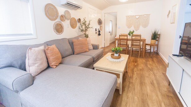 Una sala de estar moderna con un sofá gris, una mesa de centro de madera y un comedor con una mesa y sillas.