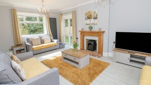 A modern living room with a sofa, coffee table, fireplace, TV, and large windows. - Morningside (Totland Bay)