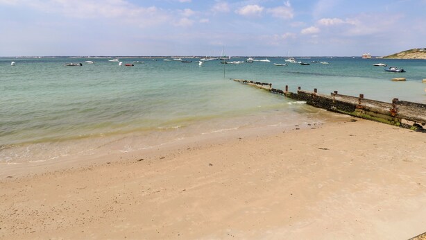 A beach with a sandy shore and a pier extending into the water. - Morningside (Totland Bay)
