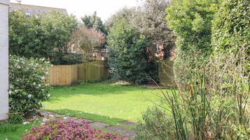 A well-maintained garden with a wooden fence, a variety of shrubs, and flowering plants.