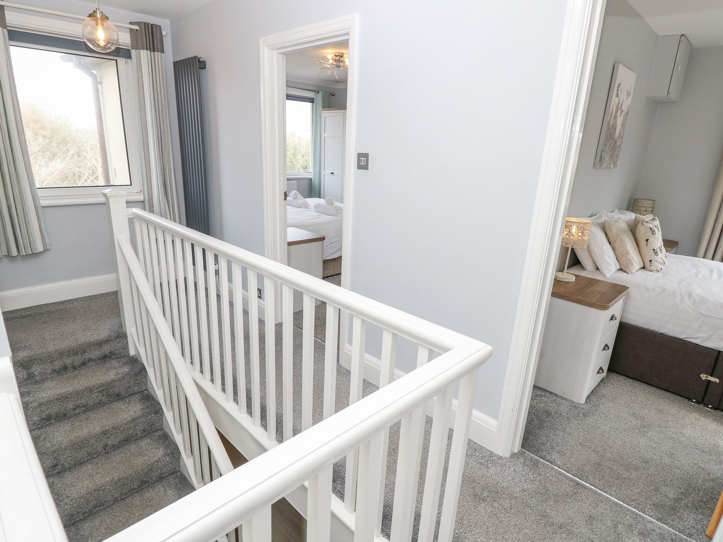 A bedroom with a bed, bedside table, and a nightstand. There is a staircase with a white railing leading to another room.