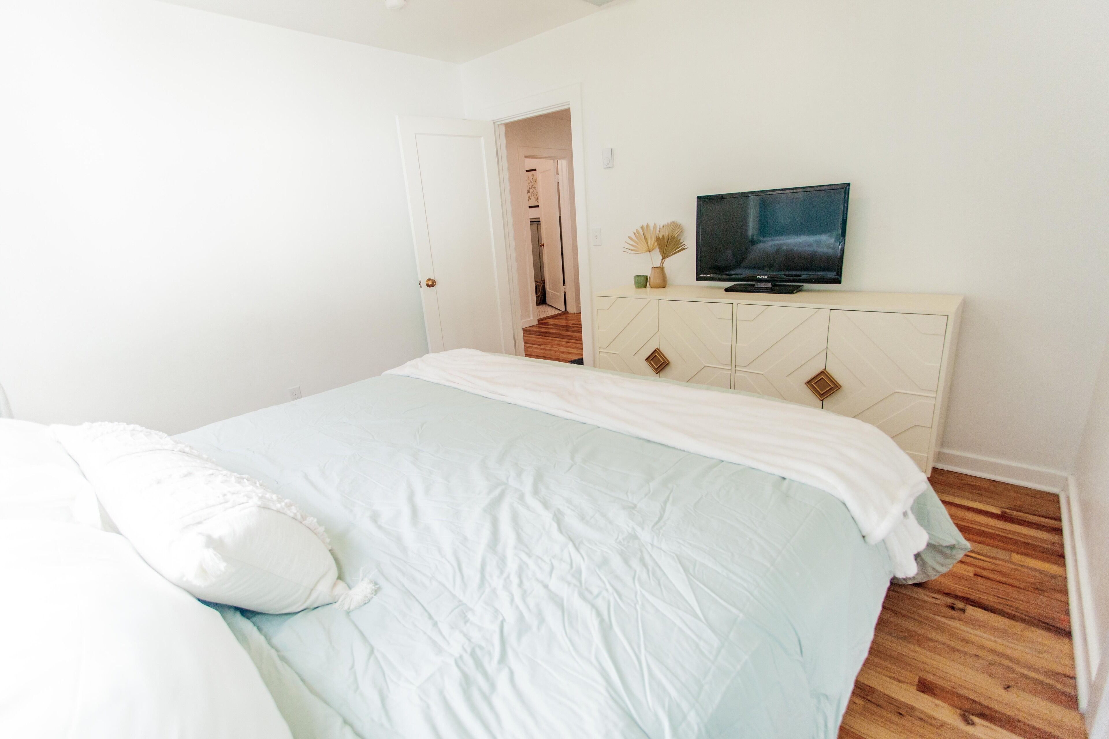 Une chambre à coucher avec un lit, un téléviseur posé sur une commode et une porte donnant sur une autre pièce.